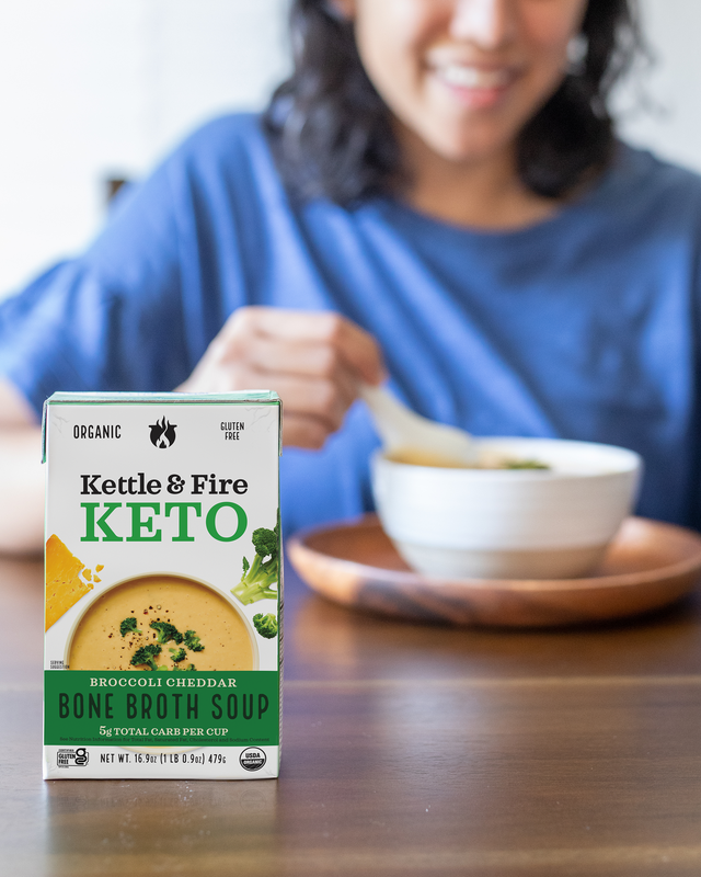Kettle & Fire broccoli cheddar bone broth soup carton with creamy soup shown in bowl behind it.