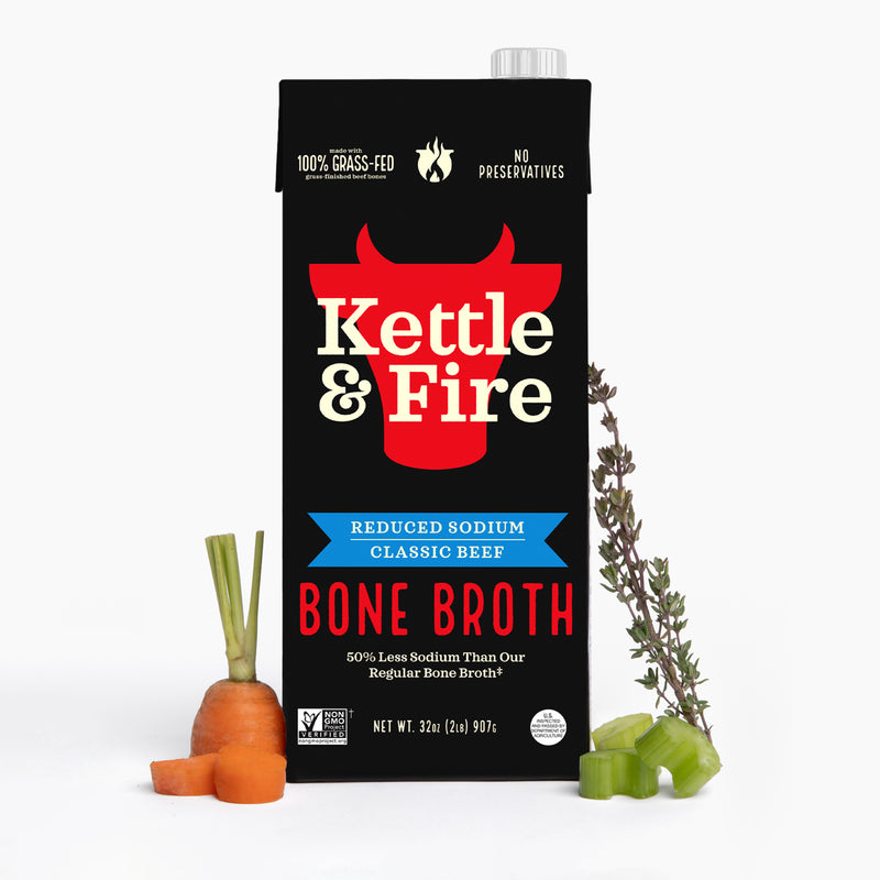 Kettle & Fire reduced sodium beef bone broth carton with carrot and herbs displayed beside it.