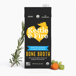 Black carton of Kettle & Fire reduced sodium chicken bone broth with rosemary sprigs and vegetables displayed beside it.